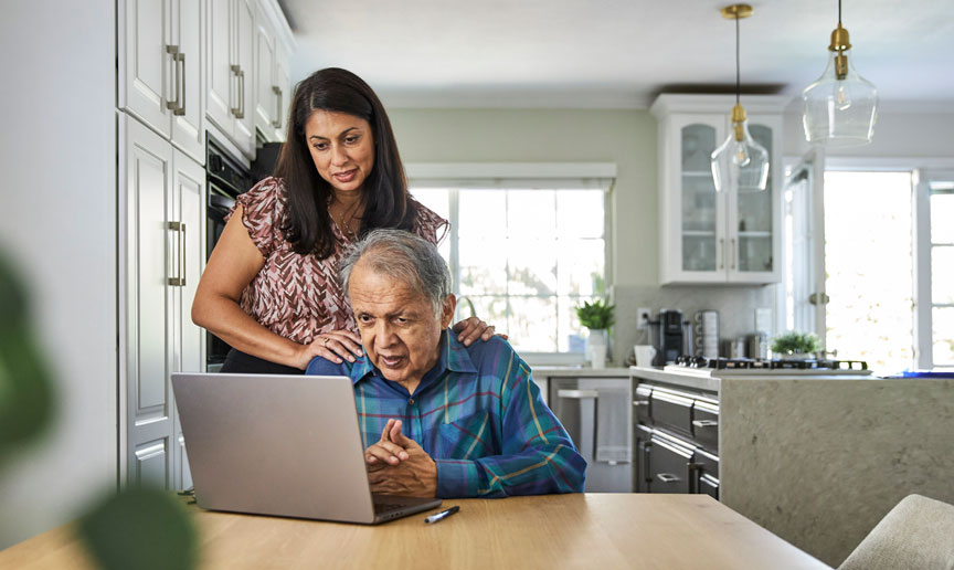 Senior parent looking at laptop with younger female shoulder surfing